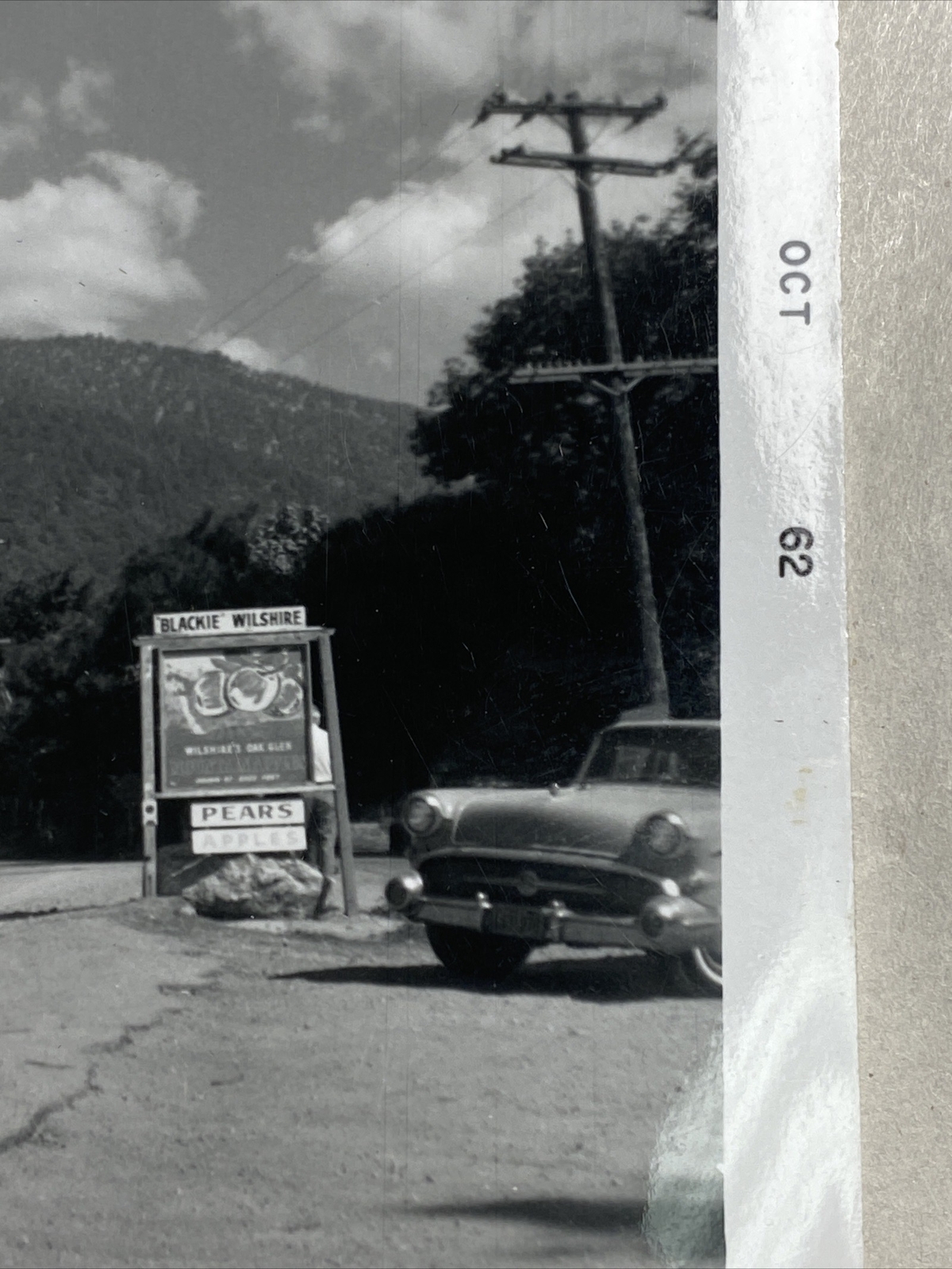 B&W Photo of an ad sign that says, « Blackie Wilshire, Pears and Apples », 1962